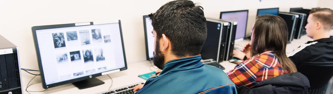 Two students sit a computers in a classroom, editing a student publication